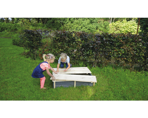 Två barn leker med en sandlåda med lock i trädgården.