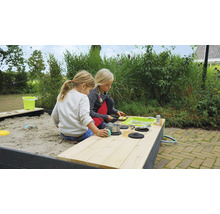 Två barn leker i en sandlåda med leksakskök i trädgården.