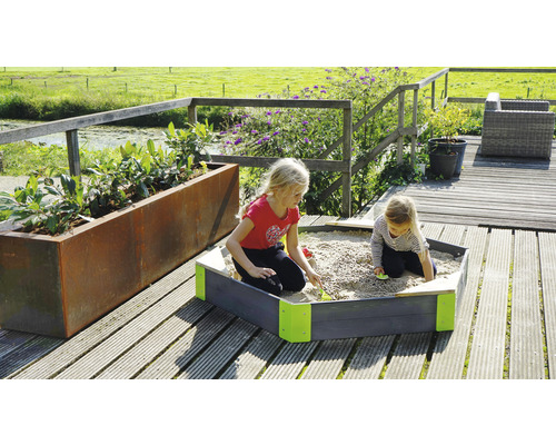 Två barn leker i sandlådan på en träaltan bredvid en blomlåda.