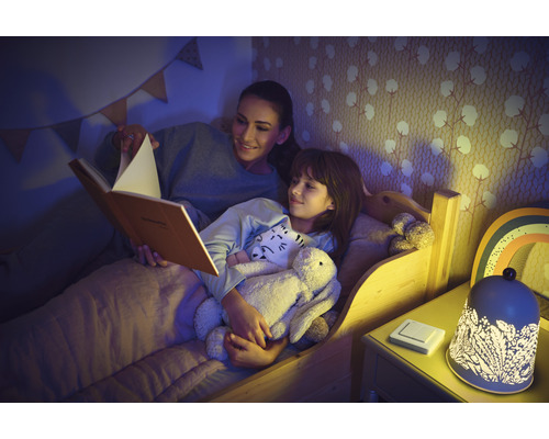 Mor läser en godnattsaga för dottern, medan en dekorativ nattlampa står på nattduksbordet.