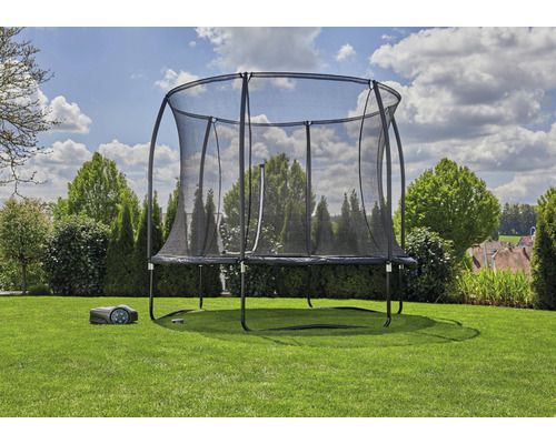 Trampolin med säkerhetsnät och robotgräsklippare i trädgården.
