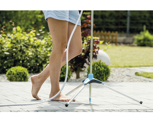 Kvinna står barfota bredvid en trädgårdsdusch på en terrass