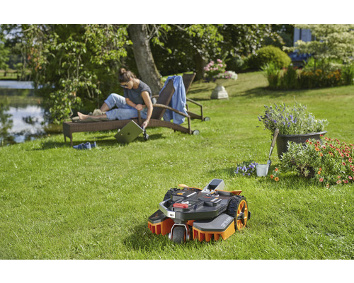 Scen med robotgräsklippare i trädgården, kvinna kopplar av på en solstol