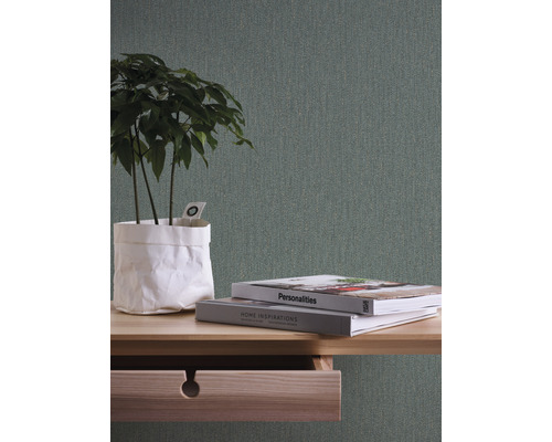 Närbild av ett bord med öppen låda, böcker och en växt på det, mot en strukturerad tapet.