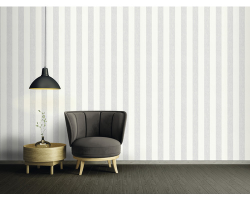 Dekorativt rum med randig tapet, fåtölj, lampa och sidobord