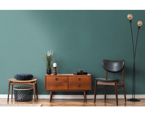 Vardagsrumsinredning med träskänk, stol, golvlampa och dekoration på parkettgolv framför en färgad vägg