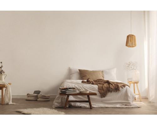 Ljust sovrum med säng, filt, kuddar, lampa, bord och dekorationer för en mysig atmosfär