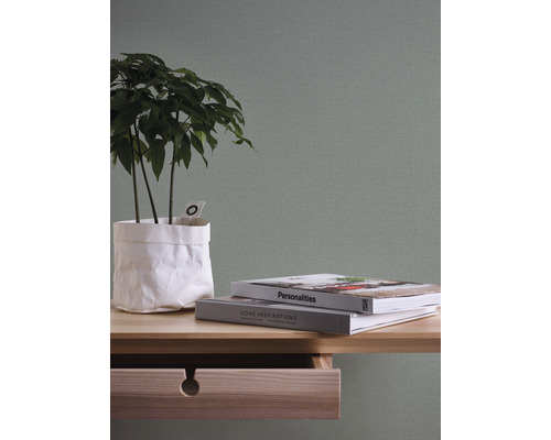 Dekorativt arrangemang med växt, böcker och trämöbler mot en enfärgad vägg.