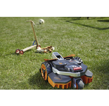 Robotgräsklippare på en gräsmatta med leksaker i bakgrunden