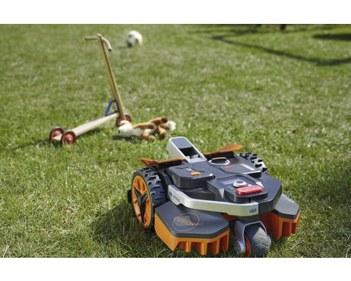 Robotgräsklippare på en gräsmatta med leksaker i bakgrunden