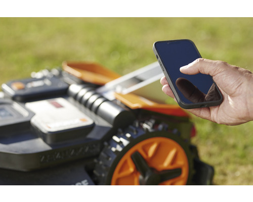 En man använder en smarttelefon för att styra en robotgräsklippare.