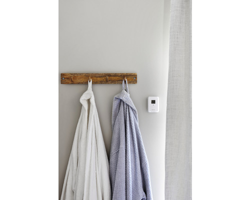 Två badrockar hänger på en träkrok bredvid en termostat på väggen.