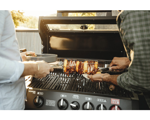 Gasolgrill med roterande grillspett och personer som grillar mat.