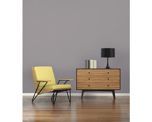 Vardagsrum med fåtölj, byrå, lampa och böcker på trägolv