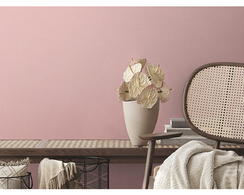 Ljus interiör med blommor i vas och rottingfåtölj framför en rosa vägg