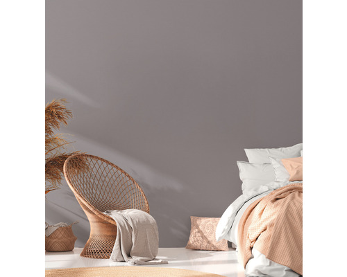 Ljust rum med rottingfåtölj, säng och dekoration för en mysig atmosfär.