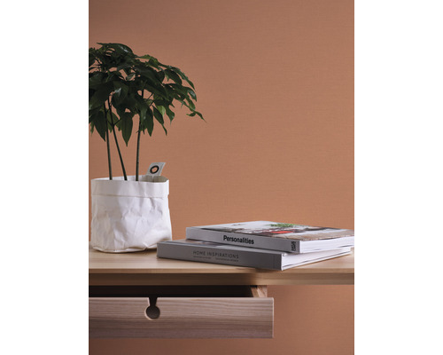 Dekorativ scen med krukväxt i en vit papperspåse, två böcker och ett träbord med öppen låda