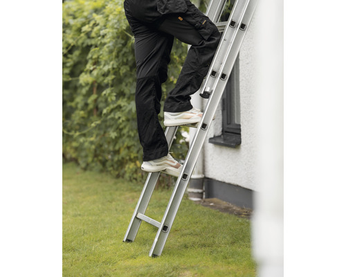 Person klättrar på en aluminiumstege framför ett hus.