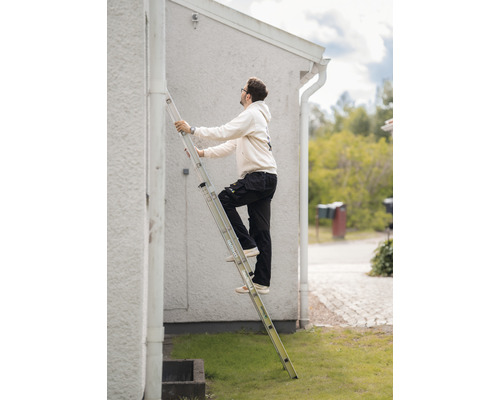 Man på en aluminiumstege framför ett hus