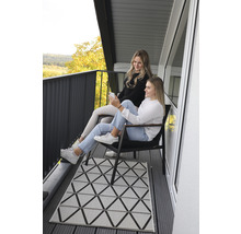 Två kvinnor sitter på en balkong med en geometrisk matta och utsikt över landskapet.