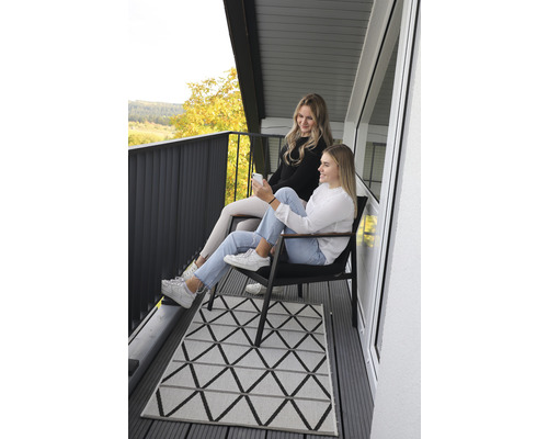 Två kvinnor sitter på en balkong med en geometrisk matta och utsikt över landskapet.