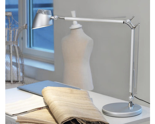 Silverfärgad skrivbordslampa på ett bord med tyger