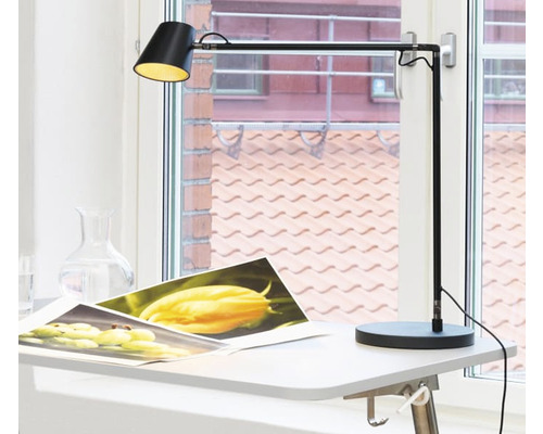 Skrivbordslampa i metall på ett bord framför ett fönster