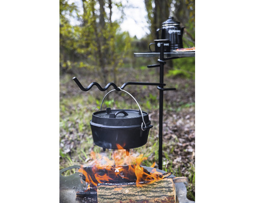 Gjutjärnspanna över öppen eld på ett stativ med campingbord och tillbehör utomhus