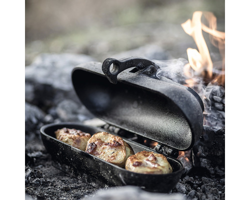 Öppen campinggrillpanna med tre potatisar vid en lägereld.