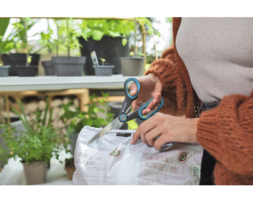 En person öppnar en förpackning med så- och kryddjord med en sax av märket Gardena.