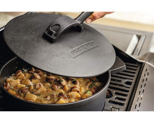 Gryta i gjutjärn med lock på en grill med mat