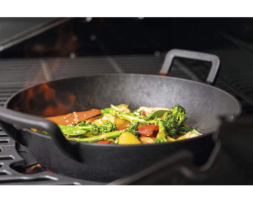 Grönsakswok på en grill med öppen låga