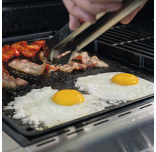 Bacon, ägg och tomater tillagas på en grillplatta med en grilltång.