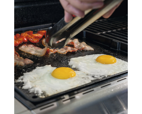 Bacon, ägg och tomater tillagas på en grillplatta med en grilltång.