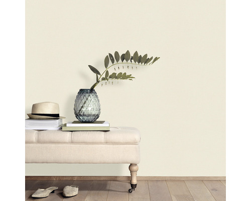 Dekorativ scen med sittbänk, vas, växter, böcker och hatt mot en vägg.