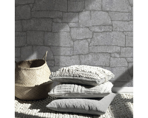 Vägg med stenmönster, korg och kuddar på en matta.