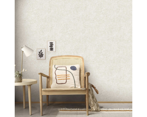 Rumsöversikt med en grov fiberduk, en stol med kudde, ett bord och dekorativa bilder på väggen.