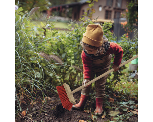 Ett barn sopar löv i trädgården med en gatusop.