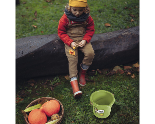 Scen med barn, pumpor i en korg och en grön hink på en gräsmatta