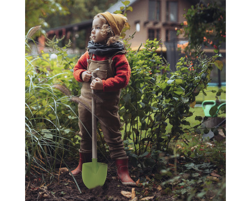 Ett barn med en spade står i trädgården.