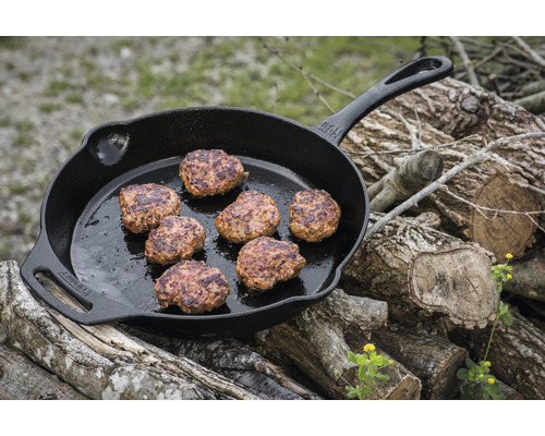 Gjutjärnspanna med hamburgare på en stapel ved