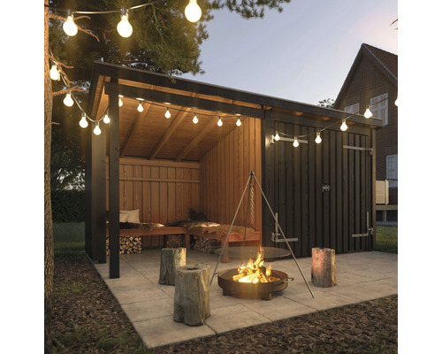 Trädgårdsskjul med belysning, eldstad och trädstamspallar på en terrass.