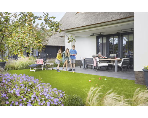 Familj spelar boule i trädgården med konstgräs, trädgårdsmöbler och växter