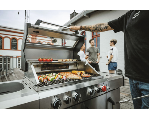 Grill i rostfritt stål med grillad mat och personer i bakgrunden
