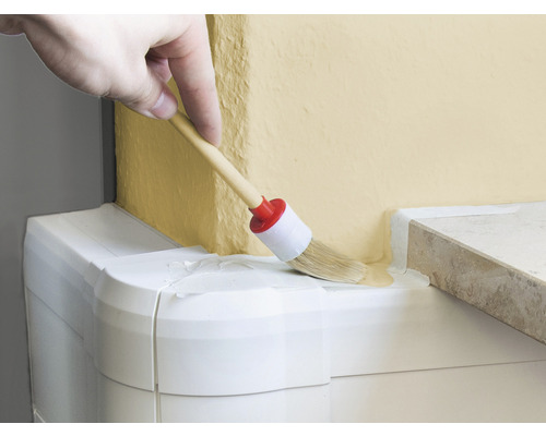 Hand målar färg på en vägg med en rund pensel.