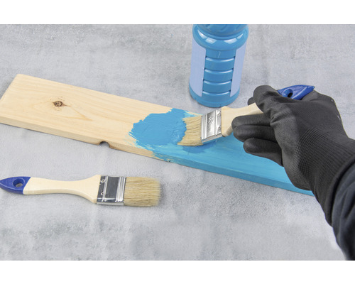 En person målar en träplanka med pensel och färg.