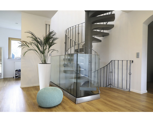 Interiörbild med spiraltrappa, glasräcke, växt i kruka och sittpuff