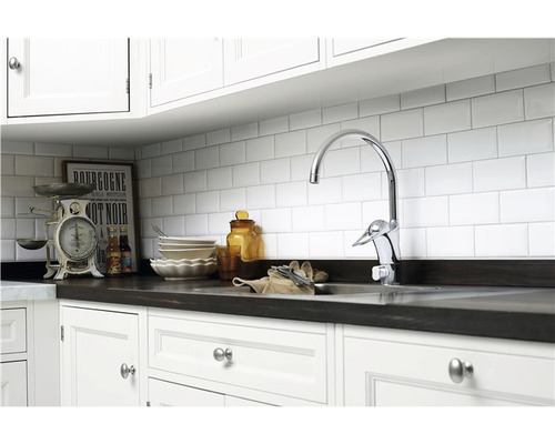 Köksscen med diskho, kran, kakelvägg och köksredskap på bänkskivan.