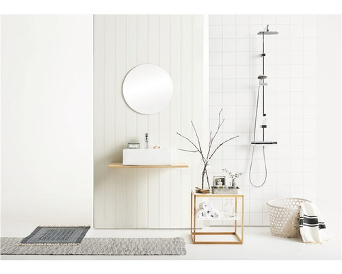 Ljust badrum med handfat, spegel, dusch och badrumsmattor