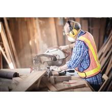 Hantverkare med cirkelsåg som sågar trä med personlig skyddsutrustning i en verkstad.